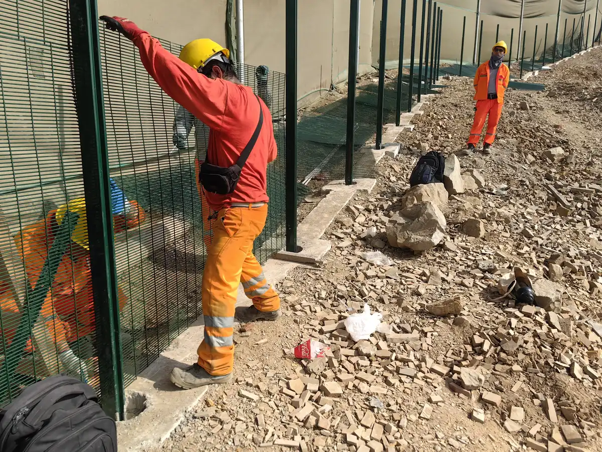 Workers installing green 358 anti-climb fence panels on concrete footings at Chancay Port