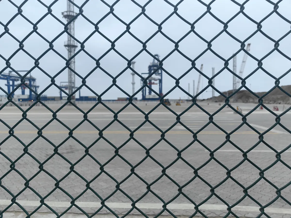 PVC-coated chain link fence with port cranes visible through the open diamond mesh